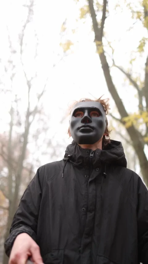 A mysterious figure in a black jacket and dark mask stands in a foggy forest, cr Stock Footage 290187342