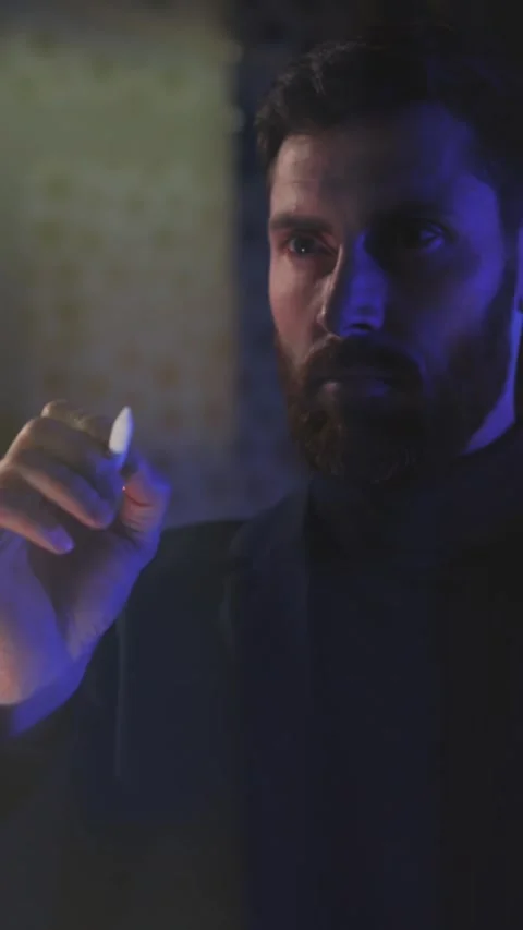 A mysterious figure is holding a cigarette while surrounded by dim light and Vídeo Stock 316523624