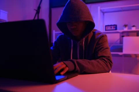 A mysterious hooded hacker working on a computer in a dark room. Stock-Fotos