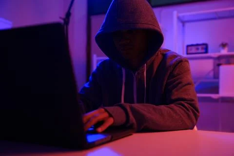 A mysterious hooded hacker working on a computer in a dark room. Foto stock