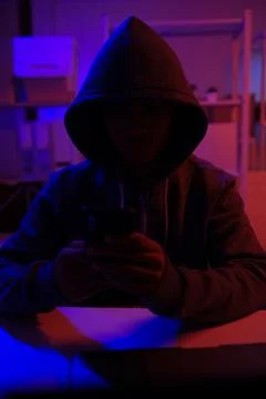 A mysterious hooded hacker working on a computer in a dark room. Stock-Fotos