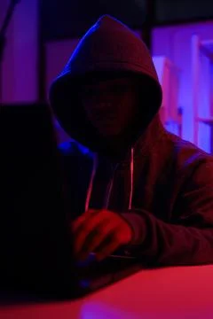 A mysterious hooded hacker working on a computer in a dark room. Stock-Fotos