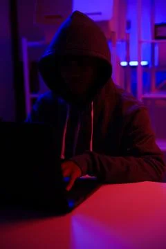 A mysterious hooded hacker working on a computer in a dark room. Foto stock