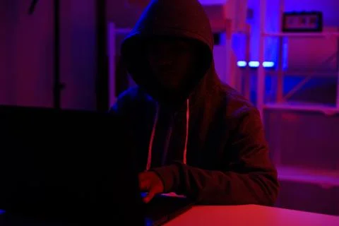 A mysterious hooded hacker working on a computer in a dark room. Stock-Fotos