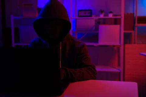 A mysterious hooded hacker working on a computer in a dark room. Stock-Fotos