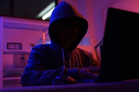 A mysterious hooded hacker working on a computer in a dark room. Stock-Fotos