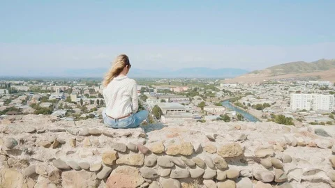 Mysterious lady with bright flying dyed hair sits on edge of stone boat on rock Stock Footage 105968697
