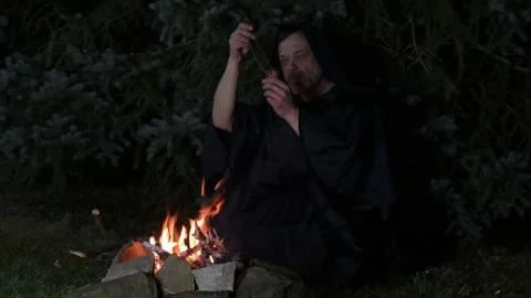 A mysterious monk in a black robe performs a ritual around a campfire in the nig Stock Footage 303783190