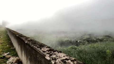 Mysterious opening scene of fog smoke rolling over a field with an old wall Stock Footage