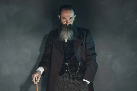 Mysterious vintage beard man in 1900 style fashion with cane against grey wal Foto stock
