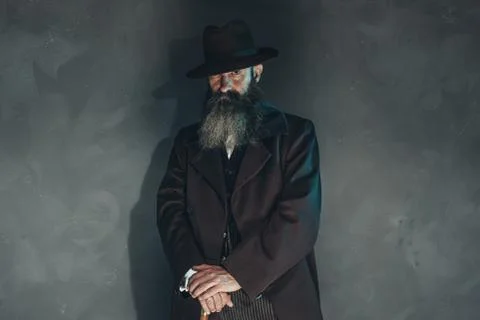 Mysterious vintage beard man in 1900 style fashion with cane against grey wal Stock Photos