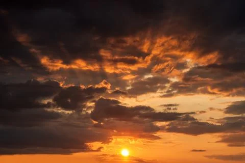 Mystical glow of sunset on a dramatic cloudy sky with the sun and rays behind Stock Photos