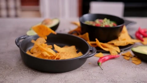 Nachos chips falling into black ceramic dish with guacamole dip sauce on Stock Footage 204603019