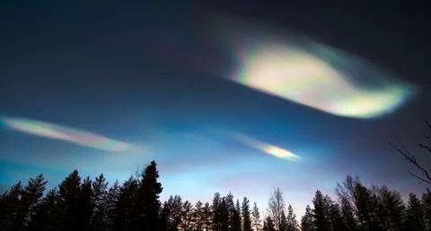 Nacreous clouds in dusk over tree silhouettes Stock Photos