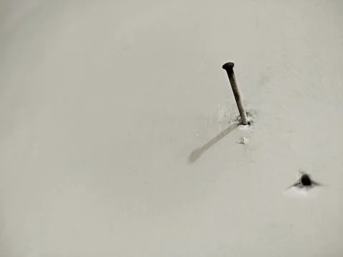 A nail embedded in the white cement wall 写真素材