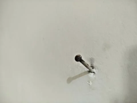 A nail embedded in the white cement wall Фото