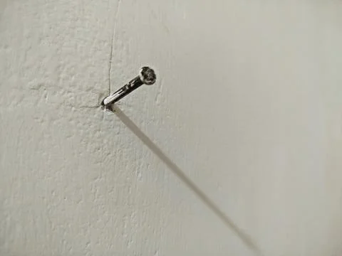 A nail embedded in the white cement wall Photos