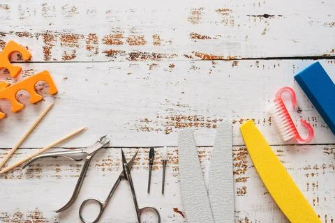 Nail files, scissors, pliers, sequins and nail polishes on a white wooden Stock Photos