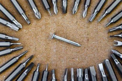 Nail surrounded by a screwdrivers bits at the bottom of a cardboard box Stock Photos