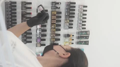 Nail technician in black gloves selecting a gel polish bottle from an organized Stock Footage 311873862