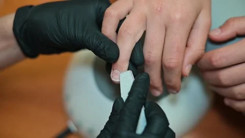 A nail technician carefully attends to a client's nails using a file to shape Video stock 338447060