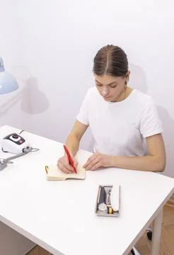 Nail technician makes notes in notebook with pen, sitting at workstation, table Stock Photos