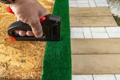 Nailing artificial grass and artificial ivy leaves to a wooden board with a.. Stock Photos