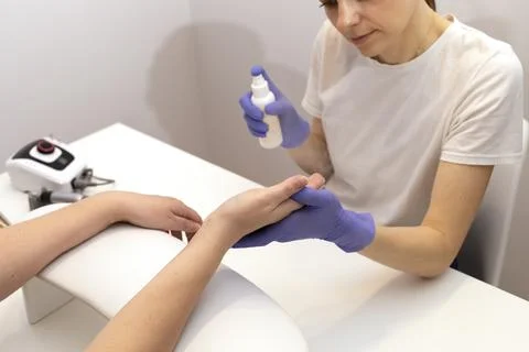 Nails master spraying, sanitizing client's hands by antiseptic from white bottle Stock Photos