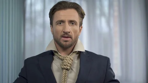 Naive handsome man fixing death rope onto suit instead of tie, implicit danger Stock Footage