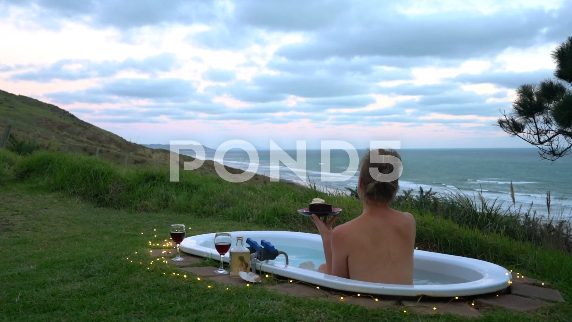 Naked woman eating cake in bath. Clifftop view.