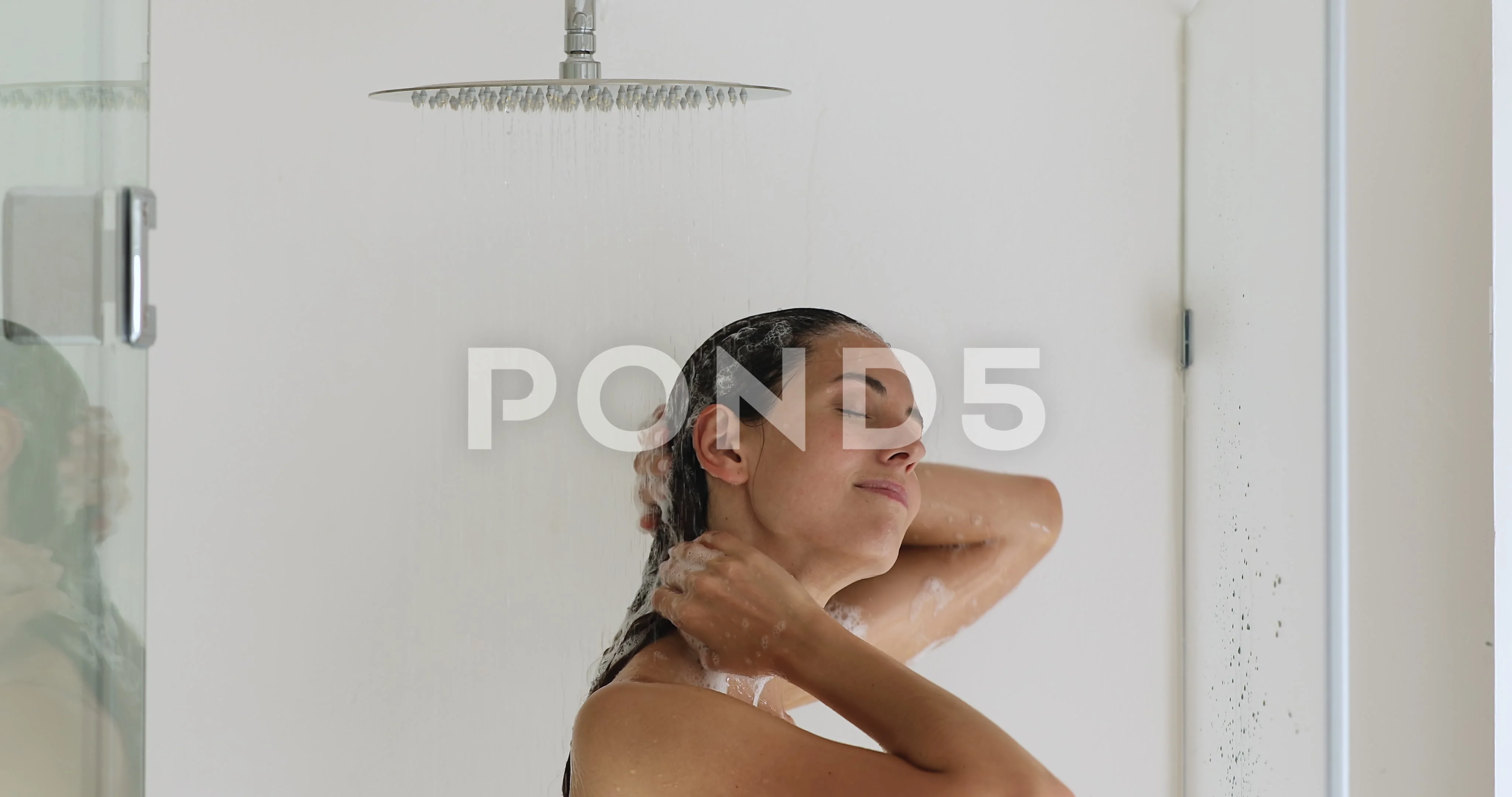 Naked woman standing under the shower washes her hair