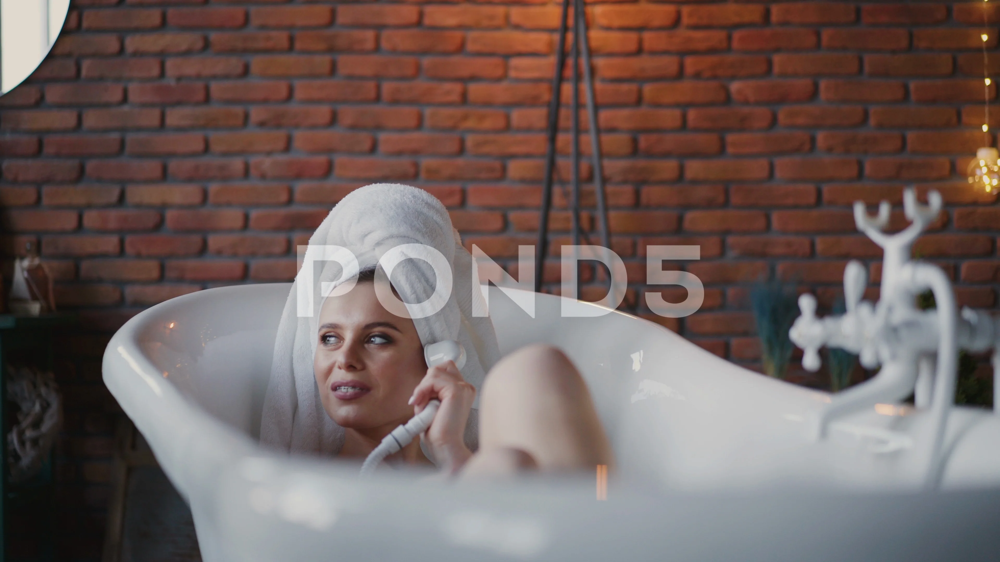 Naked woman in towel on head lying in bath and playing with shower rack