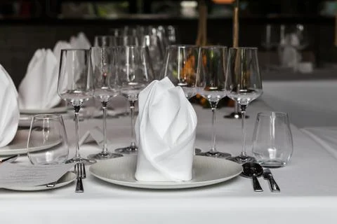 Napkin set up on dinner table with wine glass, plates, spoons, forks, knives  Stock Photos