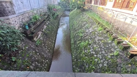 A narrow canal runs between stone walls covered in moss and vegetation. Bui.. Stock Footage 305880933