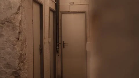 Narrow dimly lit corridor in a basement with plain white doors and exposed pipes Stock Footage 314519098