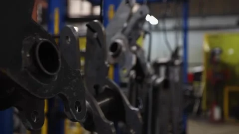 Narrow focus camera dollies past steel parts hung on hooks in factory 스톡 동영상 307194675