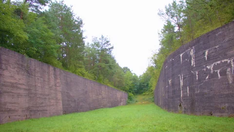 A narrow, grassy path is sandwiched between two tall, concrete walls. 스톡 동영상 305107737