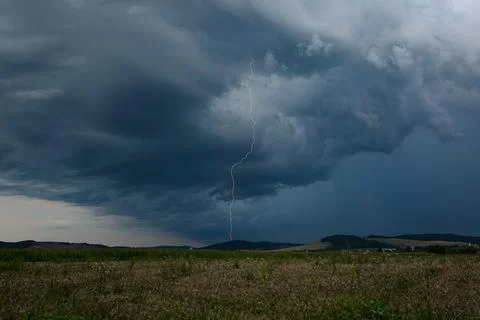 Narrow long vertical lightning bolt shoots out of a dark thundercloud Stock Photos