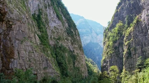 A narrow mountain gorge with a road, trees grow on steep stone slopes, cars 库存影片 256167520