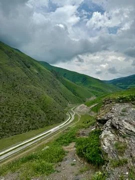 A narrow mountain road winds between green slopes in the Caucasus Mountains.. Stock Photos