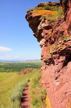 A narrow path going up the hillside along a red and high stone formation. Stock Photos