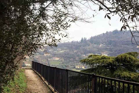 Narrow path next plants bordered by a rail in a park with hills in the back.. Stock Photos