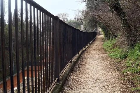 Narrow path next plants bordered by a rail in a park with hills in the back.. Stock Photos