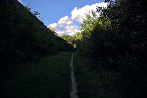Narrow path in the shade at the edge of a forest and next to a fortification  Stock Photos