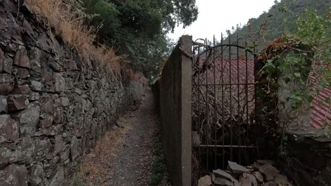 A narrow pathway runs alongside an old stone wall and a rusty metal gate Stock Footage 346294059