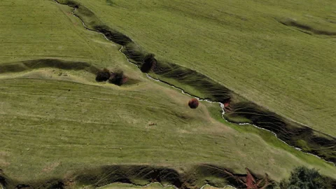 Narrow river channel crossing rolling meadow aerial view Stock Footage 324972176