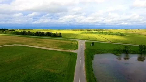 Narrow road through green fields next to calm pond Stock Footage 333836808
