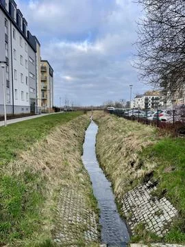 A narrow stream flows between city houses in the spring Stock Photos