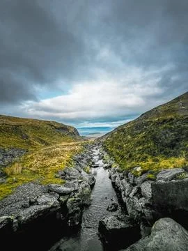 A narrow stream flows through a valley, surrounded by large rocks Stock Photos