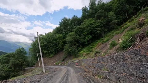A narrow unpaved road winds along a forested Georgian hillside Stock Footage 340385740